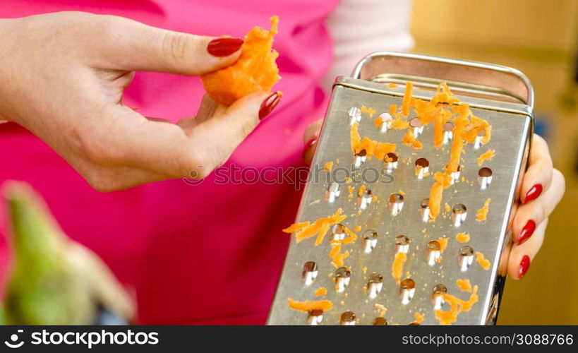 Unrecognizable woman grating carrot on metal grater, kitchen utensil making food preparing healthy vegetable salad.. Woman grating carrot on metal grater