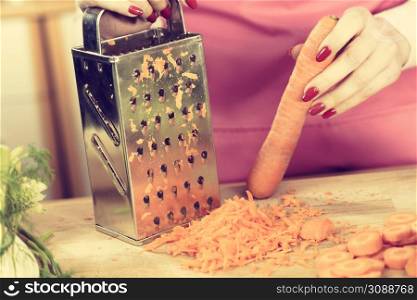 Unrecognizable woman grating carrot on metal grater, kitchen utensil making food preparing healthy vegetable salad.. Woman grating carrot on metal grater