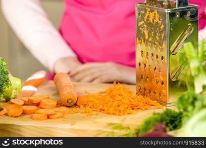 Unrecognizable woman grating carrot on metal grater, kitchen utensil making food preparing healthy vegetable salad.. Woman grating carrot on metal grater