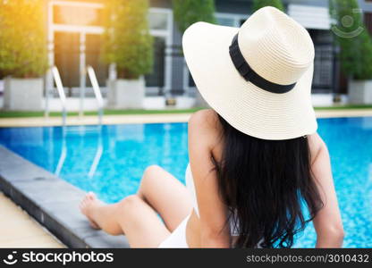 Unrecognizable woman in big hat enjoying relaxing on the swimming pool at luxury villa, travel near the sea and beach in the sunset.
