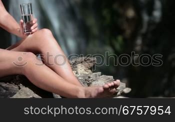 unrecognizable woman in bikini drinking a glass of mineral water near the waterfall