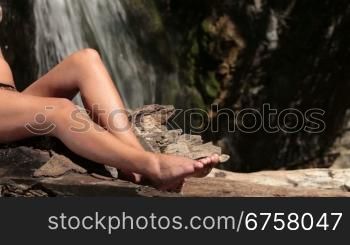 unrecognizable woman in bikini sunbathing near a waterfall