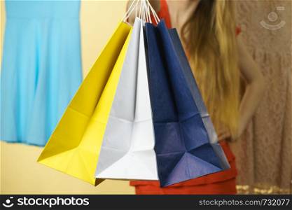 Unrecognizable woman in clothes shop store holding shopping bags picking summer perfect outfit, dress hanging on clothing hangers. Unrecognizable woman in shop picking summer outfit