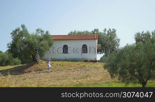 Unrecognizable woman in hat passing lawn. White building on background