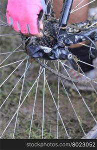 Unrecognizable woman in pink glove fixing dirty bicycle chain in close-up