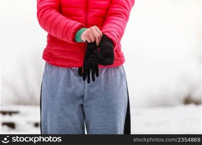 Unrecognizable woman in sportswear putting on gloves during snowy cold winter weather.. Woman putting on winter gloves