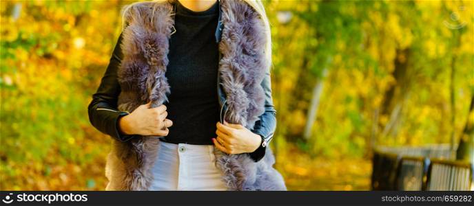 Unrecognizable woman wearing warm long dark fur vest. Autumnal fashion, autumn season styled outfits. Female having a walk in park. Woman wearing fur long vest during autumn