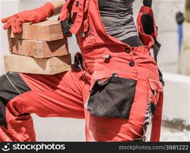 Unrecognizable woman working on construction site, building house, installing bricks. Industrial work concept.. Woman working with bricks