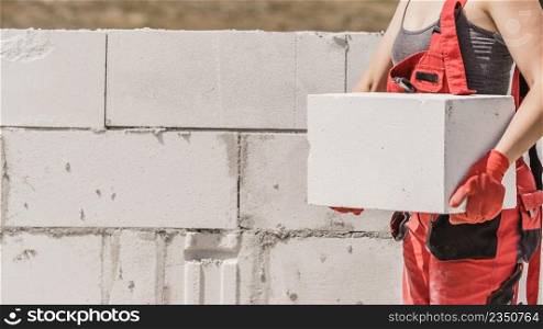 Unrecognizable woman working on construction site, building house, installing white air bricks. Industrial work concept.. Woman working with bricks