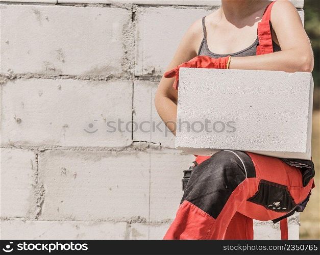 Unrecognizable woman working on construction site, building house, installing white air bricks. Industrial work concept.. Woman working with bricks