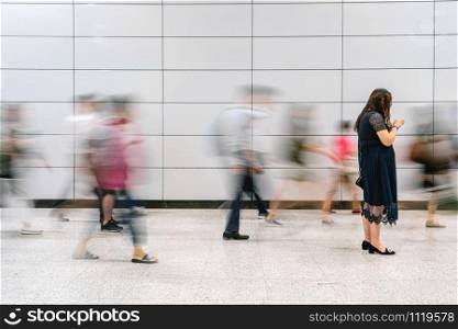 Unrecognizable working woman standing and using cellphone between moving blurred motion traveler in transportation intersection hub with white background, street photography, business commuter concept