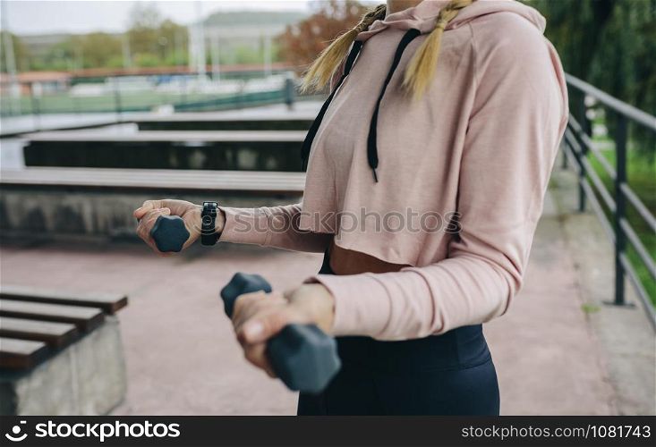 Unrecognizable young girl doing curl exercise with dumbbells outdoors. Girl training with dumbbells outdoors