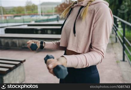 Unrecognizable young girl doing curl exercise with dumbbells outdoors. Girl training with dumbbells outdoors