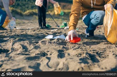 Unrecognizable young man picking up trash with group of volunteers on the beach. Young man cleaning the beach