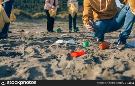 Unrecognizable young man picking up trash with group of volunteers on the beach. Young man cleaning the beach
