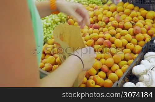 Unseen woman is picking apricots from the big pack and putting them into paper bag.