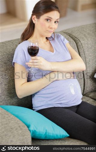 unsure pregnant woman holding a glass of red wine