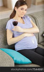 unsure pregnant woman holding a glass of red wine