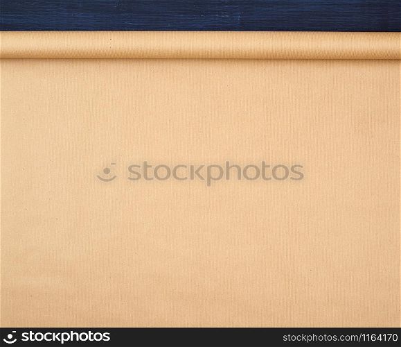 untwisted roll of brown craft paper on a blue wooden background, empty space. Old craft paper texture. Clean sheet, template