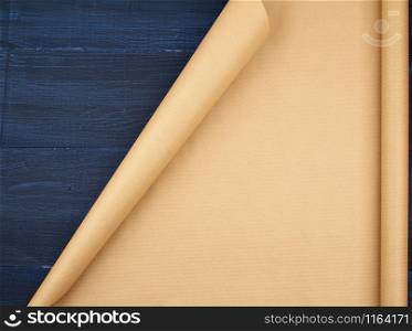 untwisted roll of brown craft paper on a blue wooden background, empty space. Old craft paper texture. Clean sheet, template, angle is twisted