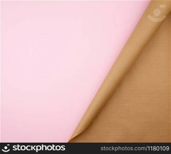 untwisted roll of brown craft paper on a pink background, empty space. Old craft paper texture. Clean sheet, template, angle is twisted