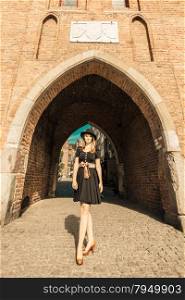 Unusual wide angle view of young woman in full length outdoors. Retro style fashion woman in black hat and dress on street of the old town european city Gdansk Danzig Poland
