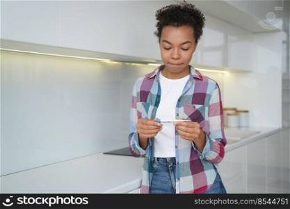 Unwanted pregnancy. Teenage girl gets in trouble with positive pregnancy test result. Frustrated african american young woman is holding stripe test and looking at it. Contraception concept.. Unwanted pregnancy. Frustrated teenage girl gets in trouble with positive pregnancy test result.