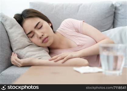 Unwell condition young Asian girl sleeping on sofa after checking temperature and taking medicines and water, Health and illness concepts