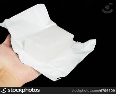 Unwrapped block of coconut fat in aluminium paper held by a person, towards black