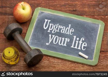 upgrade your life concept - text on slate blackboard against weathered red painted barn wood with a dumbbell, apple and tape measure