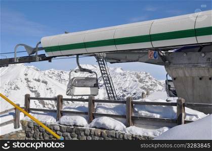 Upper station of modern chairlift for 4 persons with cabin leaving and mountains in the background - shot in Livigno, Italian Alps