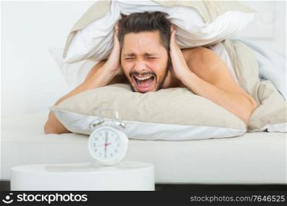 upset angry young man screaming at alarm clock on bedroom