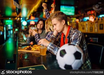 Upset football fan sitting at the counter in sports bar. Tv broadcasting, favorite team loss, game over. Upset football fan at the counter in sports bar
