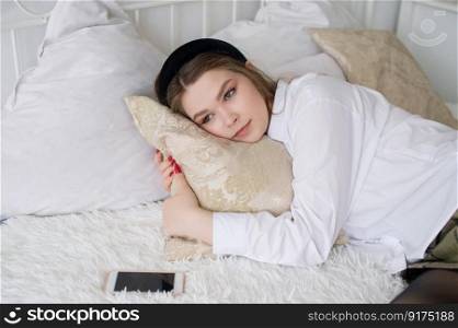 Upset girl is lying on the bed hugging a pillow next to the phone. A thoughtful girl is lying on the bed hugging a pillow next to the phone