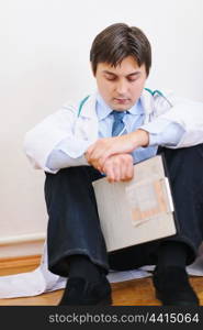 Upset male medical doctor sitting on floor