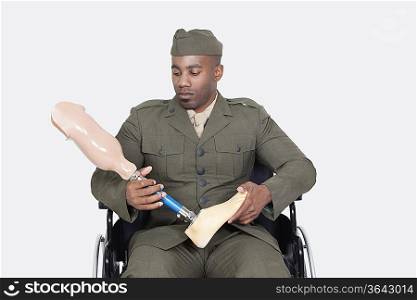 Upset military officer in wheelchair holding prosthesis leg over gray background