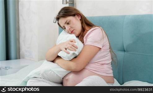 Upset pregnant woman sitting on bed and hugging big pillow. Concept of maternal and pregnancy depression. Upset pregnant woman sitting on bed and hugging big pillow. Concept of maternal and pregnancy depression.