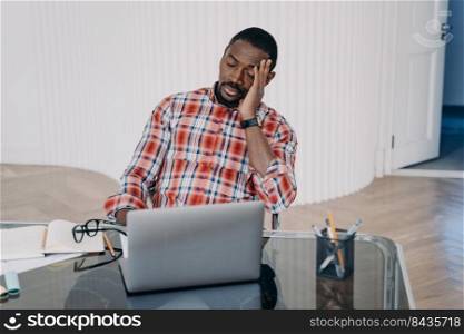 Upset tired african american businessperson hold head with hand have problem in work. Black guy businessman closed eyes sitting at office desk at laptop. Difficulties in job, professional burnout.. Upset tired african american businessman sitting at laptop suffer from headache. Difficulties in job