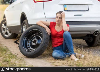 Upset woman sitting on ground at broken car