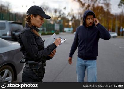 Upset young man and policewoman issuing fine ticket for wrongdoing standing on street. Upset man and police woman issuing fine