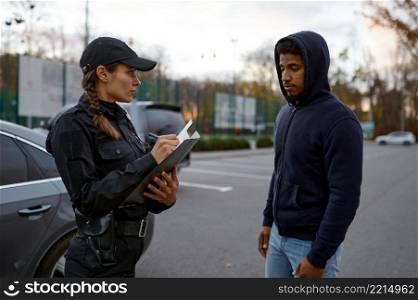 Upset young man and policewoman issuing fine ticket for wrongdoing standing on street. Upset man and police woman issuing fine