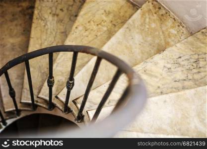 Upside view of indoor spiral winding staircase. Upside view of indoor spiral winding staircase with black metal ornamental handrail.