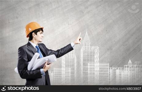 Urban construction. Young man engineer in helmet against construction project