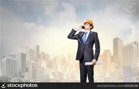 Urban construction. Young man engineer in helmet talking on mobile phone