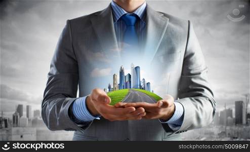 Urban development project. Close up of businessman holding city model in hands