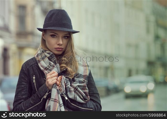 urban fashion portrait of beautiful woman , with scarf and hat , in the city street , she has freckles on face , and do her expression sweet.