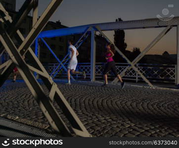 urban sports, portrait of a healthy couple jogging across the bridge in the city at early morning in night