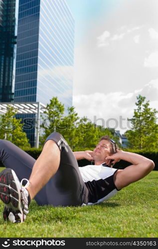 Urban sports - young man is doing warming up and sit-ups before running in the city on a beautiful summer day