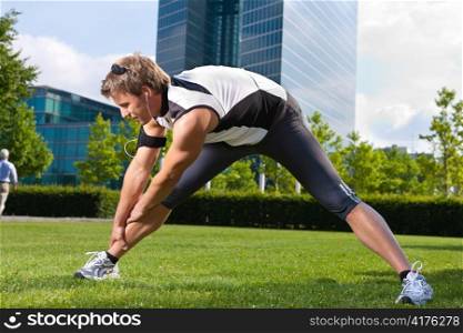 Urban sports - young man is doing warming up before running in the city on a beautiful summer day