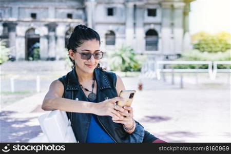 Urban style girl sitting on a bench with her cell phone, An attractive girl sitting on the cell phone smiling, Girl sitting on a bench texting on her cell phone.